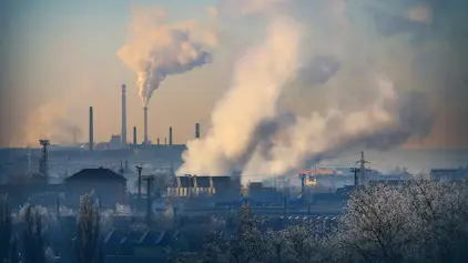 Industrielandschaft mit vielen rauchenden Schonsteinen. Der Himmel hat eine gelblich/blaue Färbung.