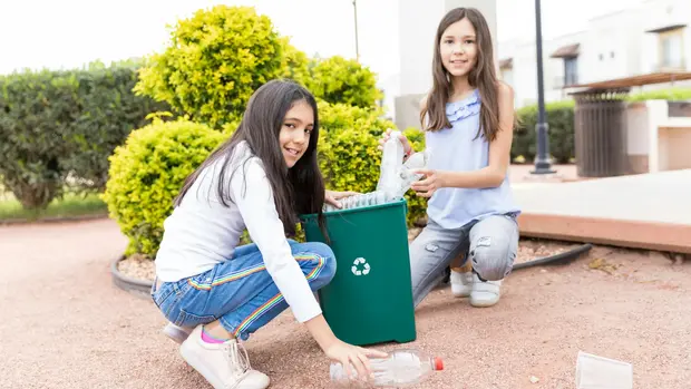 Mädchen schmeißen Plastikflaschen in einen Recyclingbehälter.