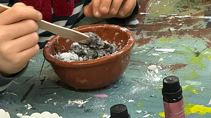 Auf einem Tisch eine Schale mit einer Masse darin, drum herum einige Fläschchen mit Ölen und Lebensmittelfarbe.