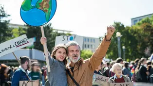 Ein Mann mit einem Kind auf dem Arm. Sie demonstrieren für das Klima, Das Kind hält ein Plakat hoch, auf dem die Erdkugel zu sehen ist.