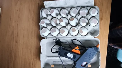 Ein Eierkarton mit Eierschalen darin und einer Heißklebepistole daneben.