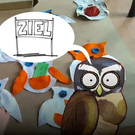 Ein Tisch mit gebastelten Eulen  - im Comic Stil hinzugefügt - eine Eule, mit einer Denkblase über dem Kopf.