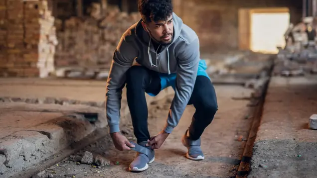 Auf dem Bild ist ein Mann zu sehen, der seinen Klettverschluss am Schuh schließt. 