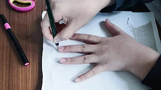 Ein Kind zeichnet die Form seiner Hand auf einem Blatt Papier nach. 