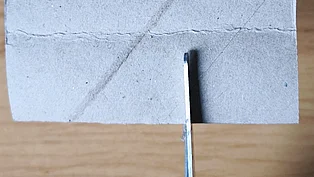 Eine Schere schneidet in ein Stück Pappe. 