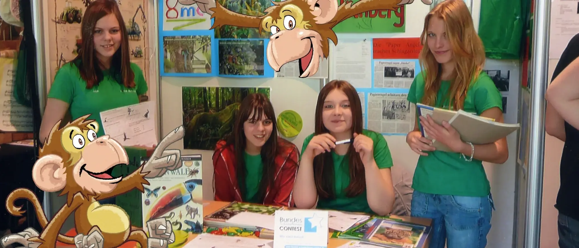 Eine Gruppe Mädchen an einem Infostand - im Comic Stil hinzugefügt - ein Affe, der auf Plakate zeigt. 