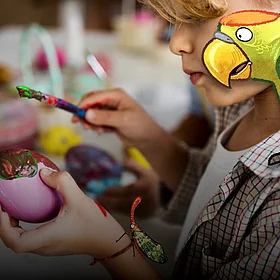 Ein Kind bemalt Ostereier mit einem Pinsel - im Comic Stil hinzugefügt - ein Papagei auf seiner Schulter und ein Käfer auf seiner Hand.