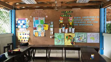 Ein Einblick in ein Klassenzimmer in Guatemala: Stühle und Tische aus Holz stehen im Raum, sodass alle einander zugewandt sind. An einer Wand hängen bunte Plakate.