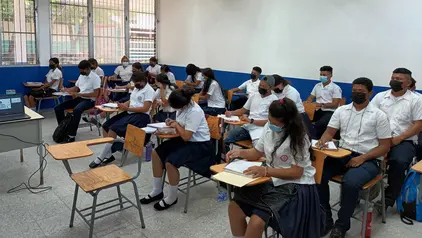 Einblick in ein Klassenzimmer in Honduras: Die Jugendlichen sitzen auf einzelnen Stühlen, an denen ein kleiner Tisch befestigt ist. Sie bearbeiten gerade eine Aufgabe.