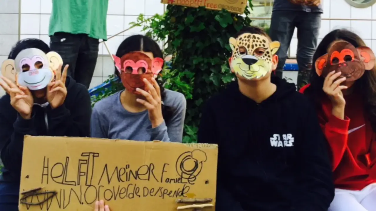 Kinder vor einem Baum, doe posen und dabei Tiermasken tragen. 