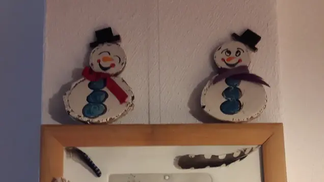 Schneemänner aus Papier, die mit einer Prickelnadel ausgestochen wurden, hängen an der Wand.