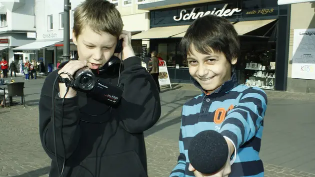 Kinder in Aktion: 2 Kinder führen ein Interview mit Mikro und Kamera. 