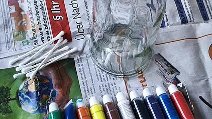 Bastelzubehör: eine Glasvase, Acrylfarben und Wattenstäbchen. 