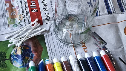 Bastelzubehör: eine Glasvase, Acrylfarben und Wattenstäbchen. 