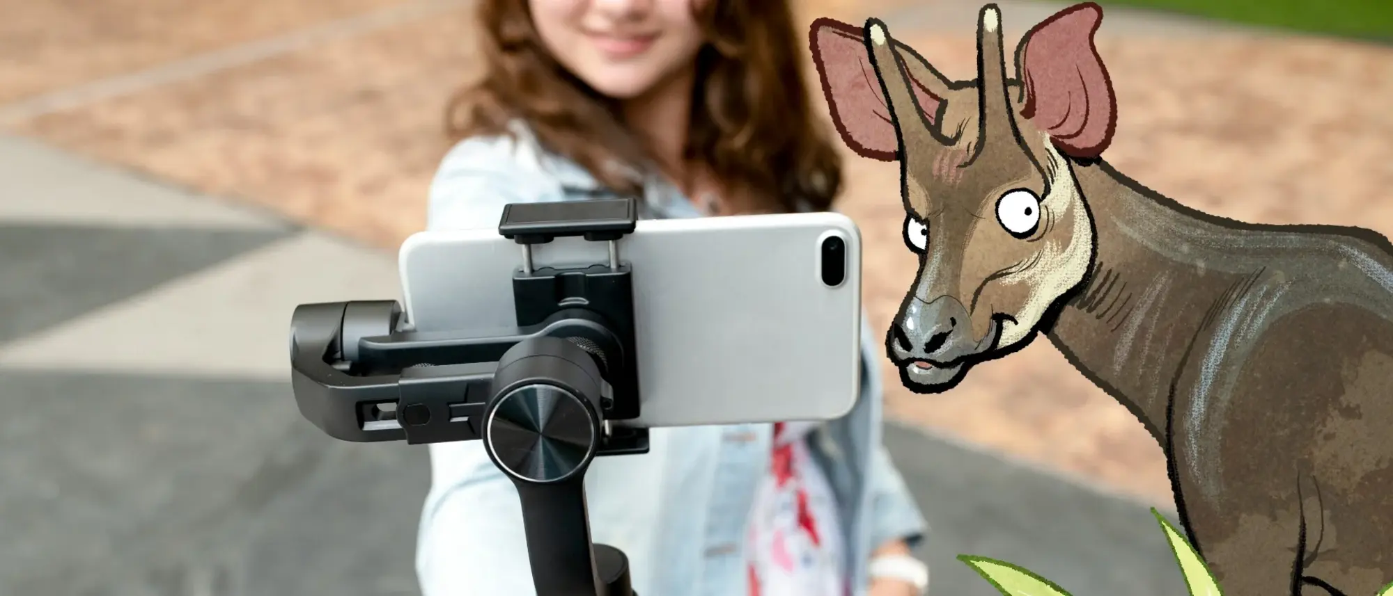 Das Bild zeigt ein Mädchen, dass in eine Handykamera lächelt  - im Comic Stil hinzugefügt - ein Okapi und eine Grünpflanze neben dem Mädchen.. 