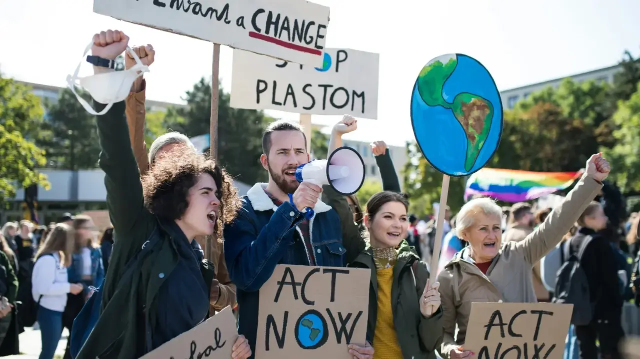 Vier Personen mit Schildern und einem Megafon demonstrieren mit erhobenen Händen für eine gesunde Erde. 