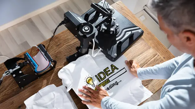 Shirtdruck im Copyshop ©Andrey Popov/iStock Eine Person bedruckt ein T-Shirt mit einer Druckmaschine.
