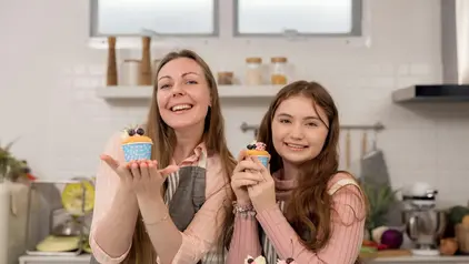 Kuchen vorbereiten ©GettyImages/unsplashplus Eine Frau und ein Mädchen halten frisch gebackene Muffins in die Kamera.