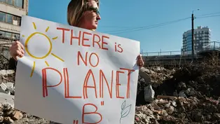 Eine Frau hält ein Demoschild hoch auf dem steht: „There is no planet B“.