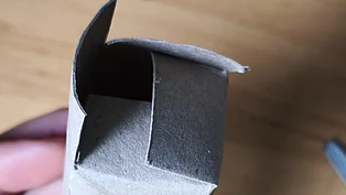 Eine Toilettenpapierrolle wird gefaltet, um einen Eierbecher daraus zu formen. 