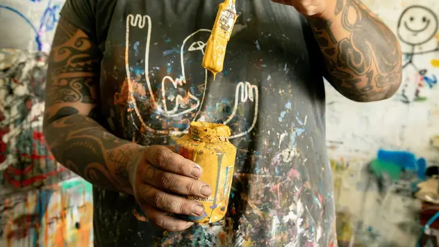 Shirt selber bemalen ©Molly the Cat/unsplashplus Eine Hand hält ein Glas voll Farbe vor der Brust. Darüber ein farbgetränkter Pinsel.