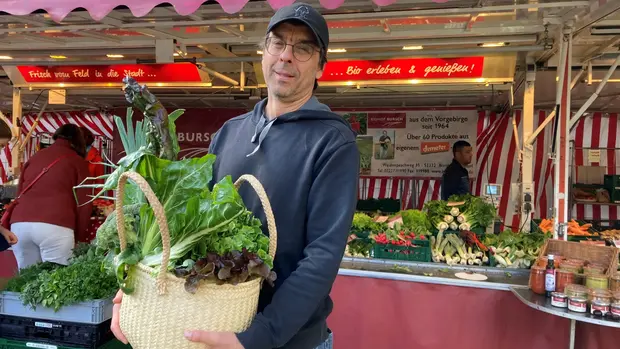 Das Bild zeigt Uli vor dem Marktstand. Saisonal und regional einkaufen geht am besten auf dem Wochenmarkt. Jede Stadt hat einen solchen Markt. Dort bieten Bauern ihre Ernte an. 