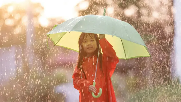 Ein Mädchen schützt sich mit einem gelben Regenschirm vor dem Regen 