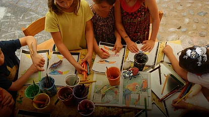 Kinder basteln an einem Tisch mit Papier - im Comic Stil hinzugefügt - mehrere Käfer und ein Äffchen.