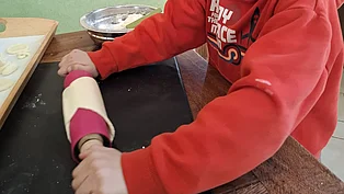 Ein Junge rollt Teig mit einem Nudelholz aus. 