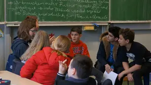 Schüler*innen sitzen in einem Klassenzimmer und diskutieren über Umweltthemen. 