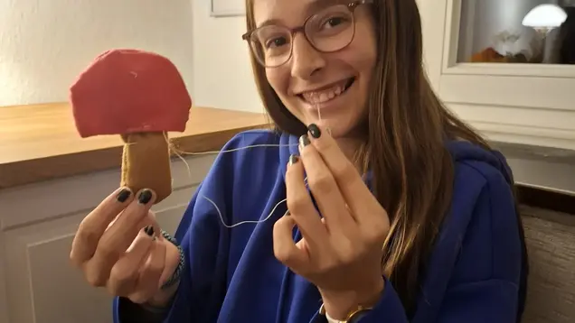 Ein Mädchen näht einen Fliegenpilz aus Filz. 