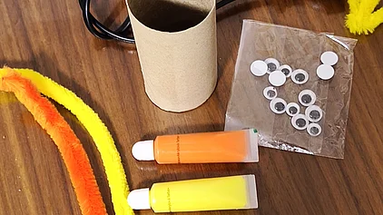 Bastelutensilien: Toilettenpapierrolle, Farbe, Pfeifenputzer, Augen und eine Heißklebepistole. 